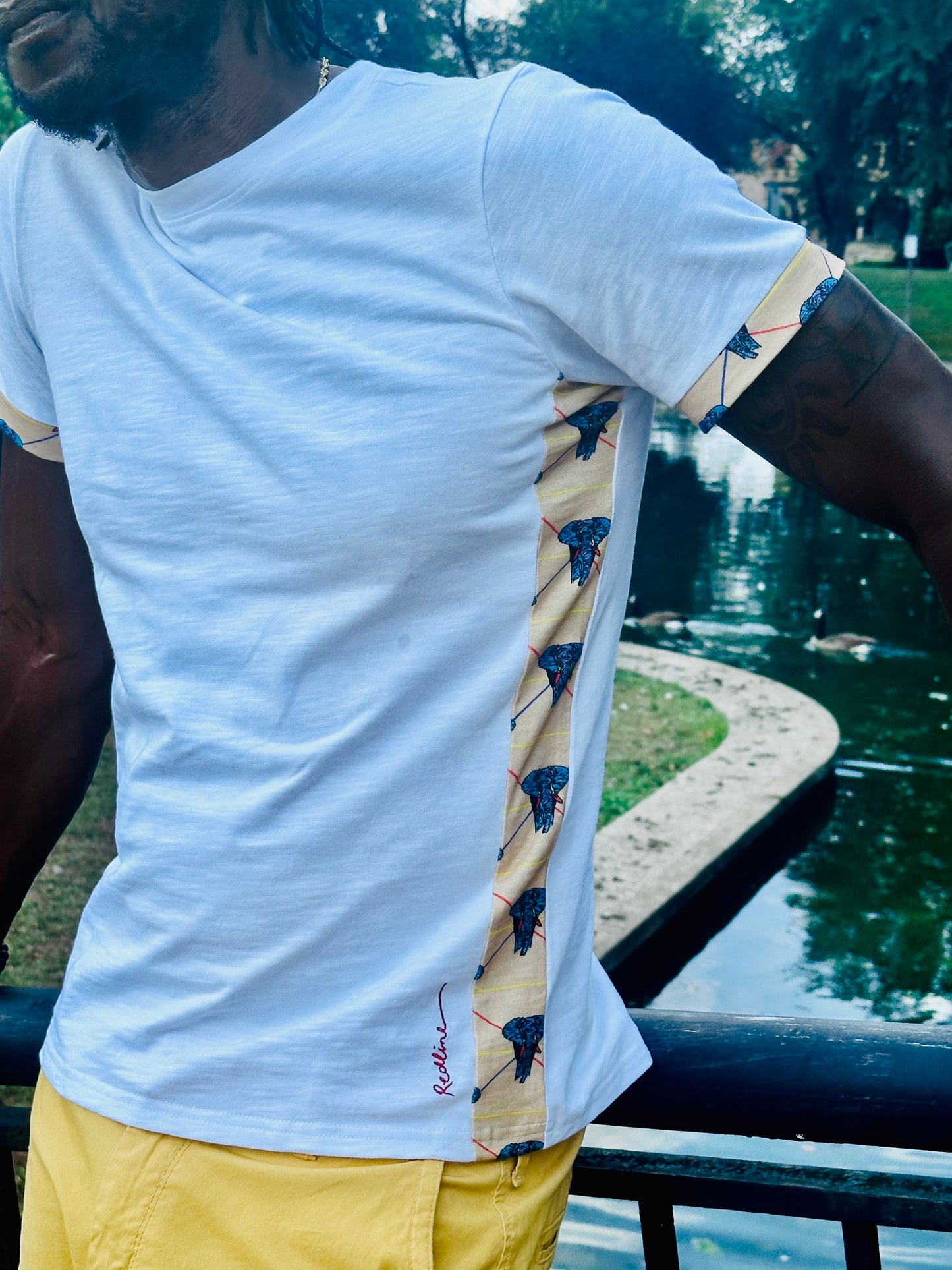 Person wearing a white t-shirt with patterned sleeves and yellow shorts, standing by a body of water.